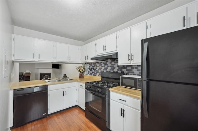 kitchen with light countertops, under cabinet range hood, a sink, light wood finished floors, and black appliances