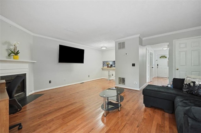 living room with crown molding, visible vents, wood finished floors, baseboards, and a fireplace with flush hearth