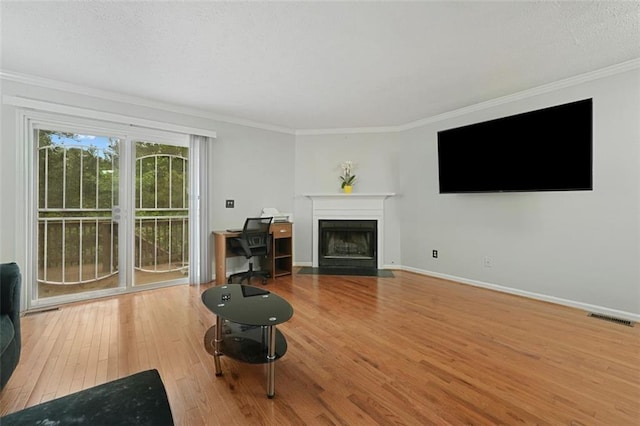 living area featuring visible vents, ornamental molding, hardwood / wood-style floors, baseboards, and a fireplace with flush hearth
