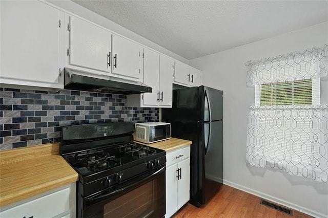 kitchen with light countertops, under cabinet range hood, light wood finished floors, backsplash, and black appliances