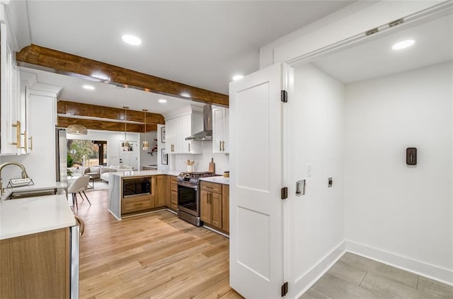 kitchen featuring stainless steel gas range, wall chimney range hood, built in microwave, a sink, and light wood-type flooring