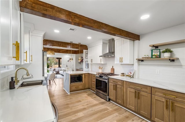 kitchen featuring stainless steel gas range, wall chimney range hood, built in microwave, a sink, and beam ceiling