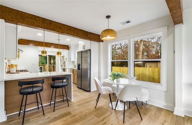 kitchen with stainless steel refrigerator with ice dispenser, a peninsula, white cabinets, light wood finished floors, and plenty of natural light
