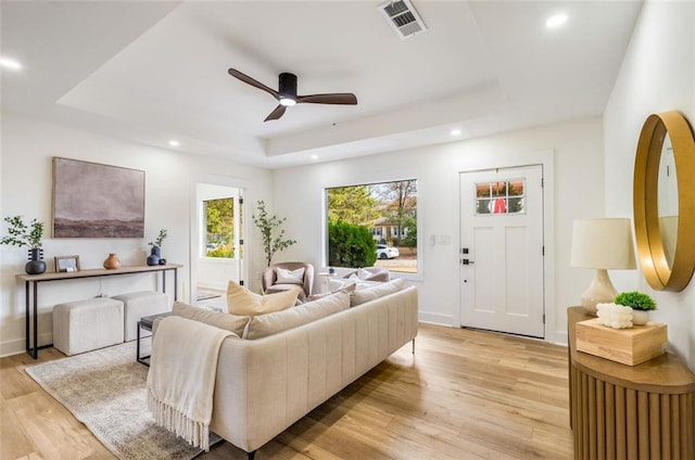 living room with a tray ceiling, light wood-type flooring, recessed lighting, a ceiling fan, and baseboards