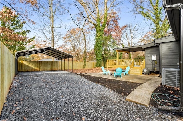fenced backyard with a detached carport, central AC, driveway, and a wooden deck