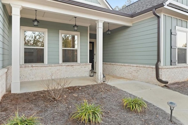 view of exterior entry featuring covered porch, brick siding, roof with shingles, and board and batten siding