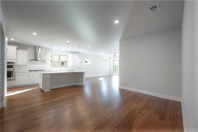 kitchen with a center island, wall chimney range hood, dark hardwood / wood-style flooring, pendant lighting, and white cabinets