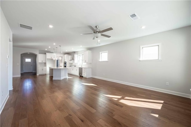 unfurnished living room with ceiling fan, dark wood-type flooring, and a healthy amount of sunlight