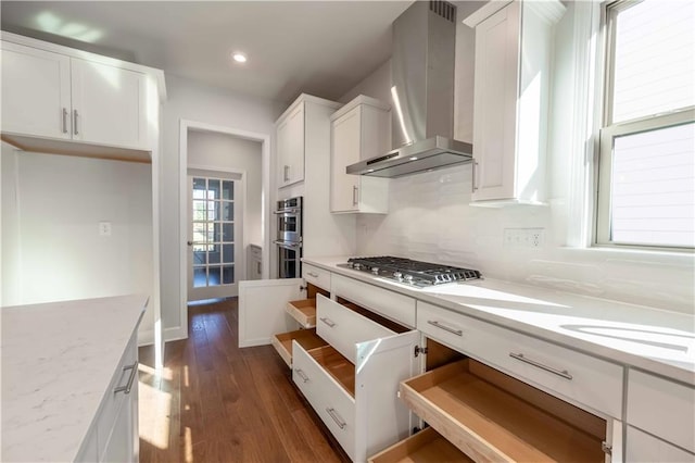 kitchen featuring light stone countertops, wall chimney exhaust hood, stainless steel appliances, dark wood-type flooring, and white cabinetry