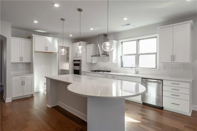 kitchen featuring white cabinets, a kitchen island, wall chimney range hood, and stainless steel appliances