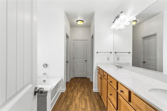 full bathroom with double vanity, a bath, wood finished floors, and a sink