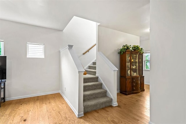 stairway featuring baseboards, a healthy amount of sunlight, and wood finished floors