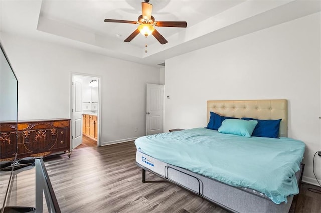 bedroom featuring a raised ceiling, a ceiling fan, baseboards, ensuite bathroom, and wood finished floors
