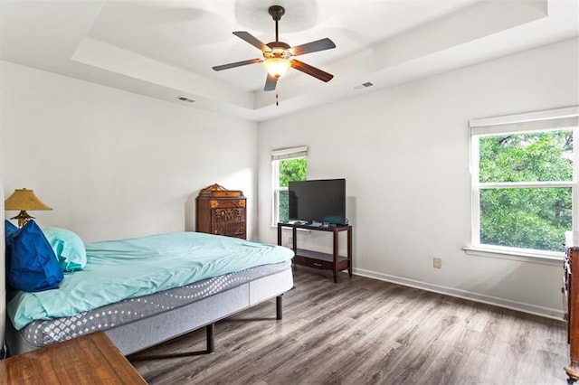 bedroom featuring visible vents, baseboards, wood finished floors, and a tray ceiling