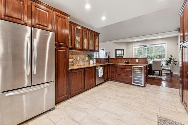 kitchen featuring kitchen peninsula, appliances with stainless steel finishes, backsplash, light stone counters, and beverage cooler