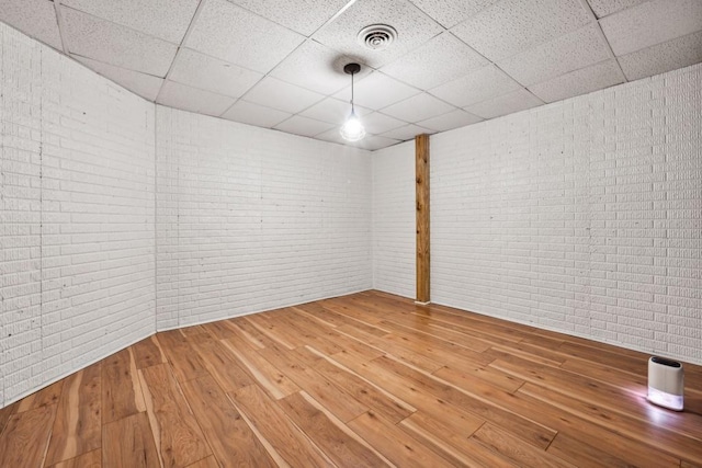 unfurnished room featuring a paneled ceiling, brick wall, and hardwood / wood-style flooring