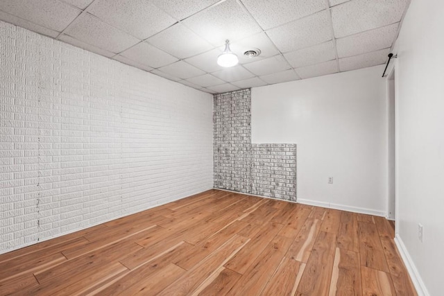 spare room featuring hardwood / wood-style floors, a paneled ceiling, and brick wall