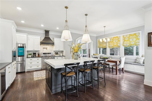 kitchen with white cabinets, a kitchen island, custom exhaust hood, stainless steel appliances, and hanging light fixtures