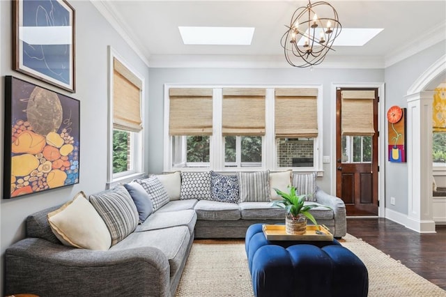 living room featuring a skylight, dark hardwood / wood-style flooring, ornamental molding, and an inviting chandelier