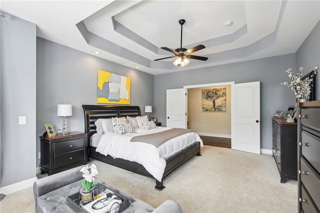 bedroom with a raised ceiling, ceiling fan, and light carpet