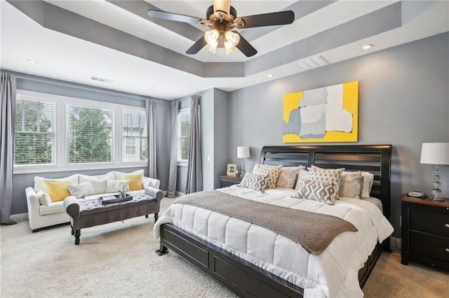 carpeted bedroom with ceiling fan, a raised ceiling, and multiple windows