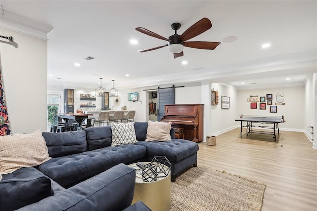 living room featuring ceiling fan, light hardwood / wood-style flooring, crown molding, and a barn door