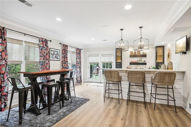 bar with wood-type flooring, ornamental molding, a chandelier, and hanging light fixtures