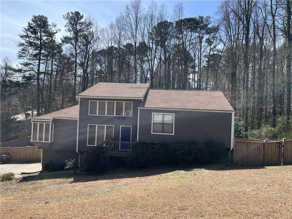 view of front of house with a front lawn, fence, and a shingled roof