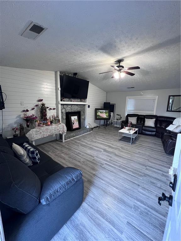 living room with ceiling fan, wood walls, hardwood / wood-style floors, a textured ceiling, and a fireplace