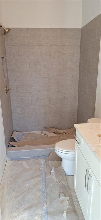 bathroom featuring vanity, a tile shower, and toilet