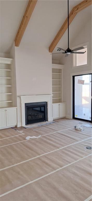 unfurnished living room with beamed ceiling, ceiling fan, high vaulted ceiling, and built in shelves