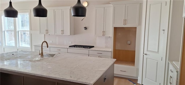 kitchen featuring a kitchen island with sink, gas stovetop, light stone countertops, and white cabinets