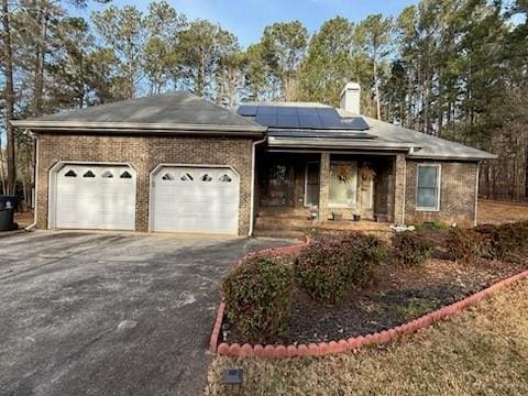 ranch-style house with solar panels, an attached garage, a chimney, aphalt driveway, and brick siding