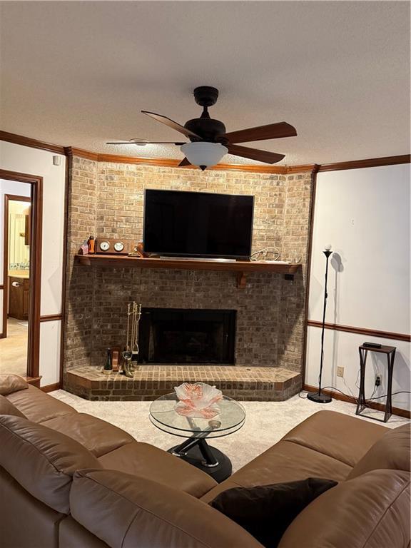 carpeted living area featuring ceiling fan, a textured ceiling, a brick fireplace, and ornamental molding