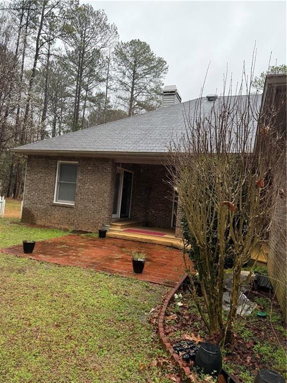 back of house with brick siding, a chimney, a yard, and roof with shingles