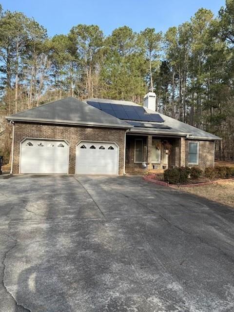 ranch-style house featuring brick siding, solar panels, aphalt driveway, a chimney, and a garage