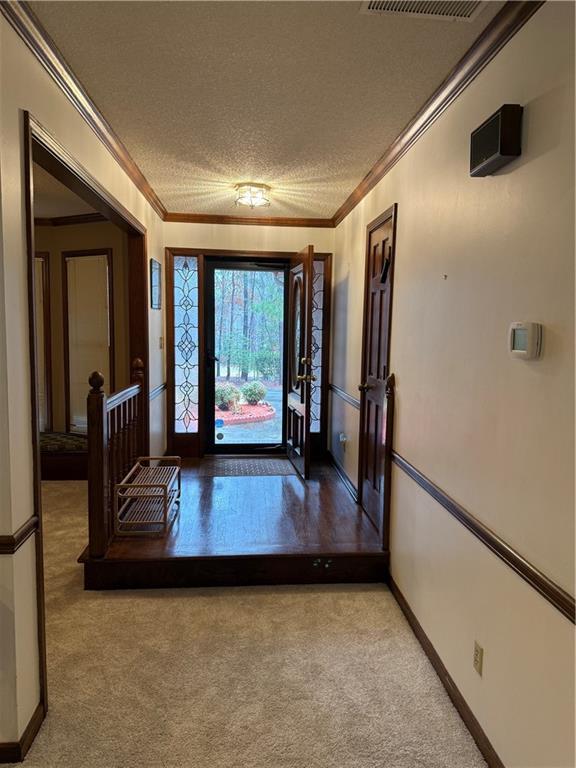 foyer featuring crown molding, light colored carpet, baseboards, and a textured ceiling