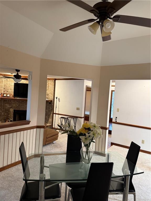 carpeted dining area featuring lofted ceiling, a brick fireplace, a ceiling fan, and baseboards