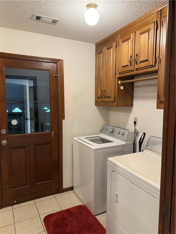 laundry area featuring visible vents, light tile patterned floors, washer and dryer, cabinet space, and a textured ceiling