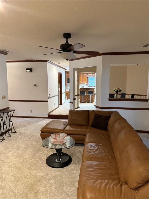 living area featuring visible vents, ornamental molding, carpet floors, baseboards, and ceiling fan