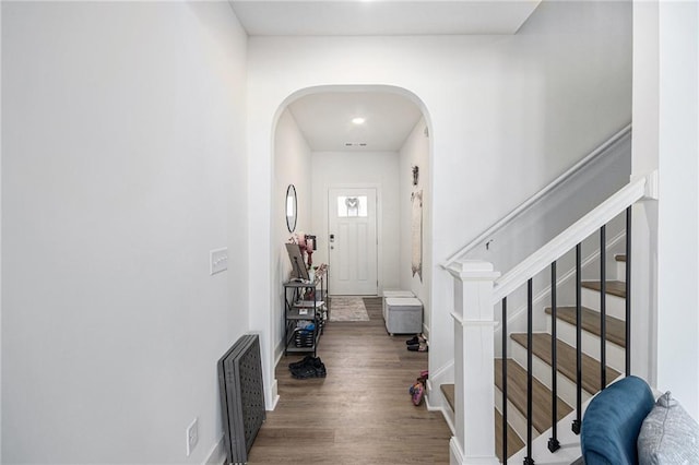 interior space featuring arched walkways, wood finished floors, stairs, and baseboards