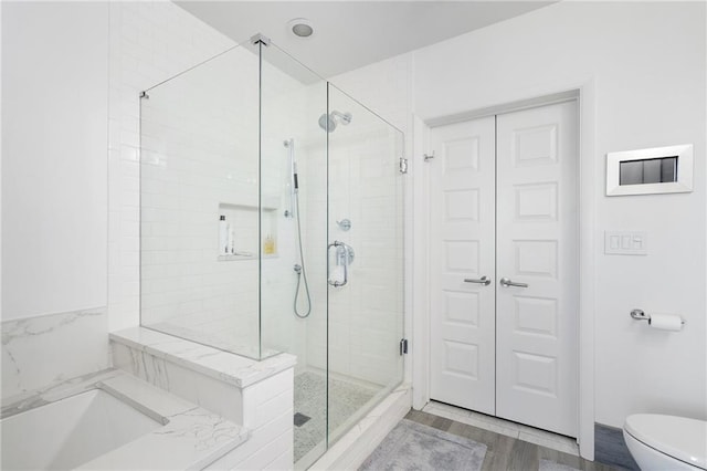 bathroom featuring a garden tub, toilet, wood finished floors, and a shower stall