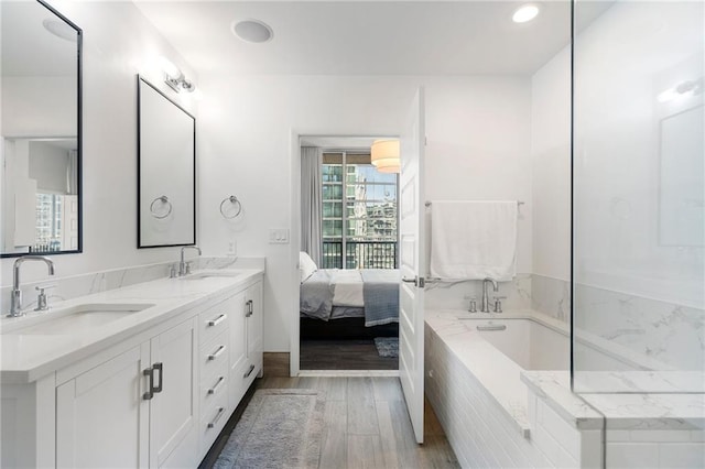 bathroom with a sink, ensuite bath, wood finished floors, and double vanity