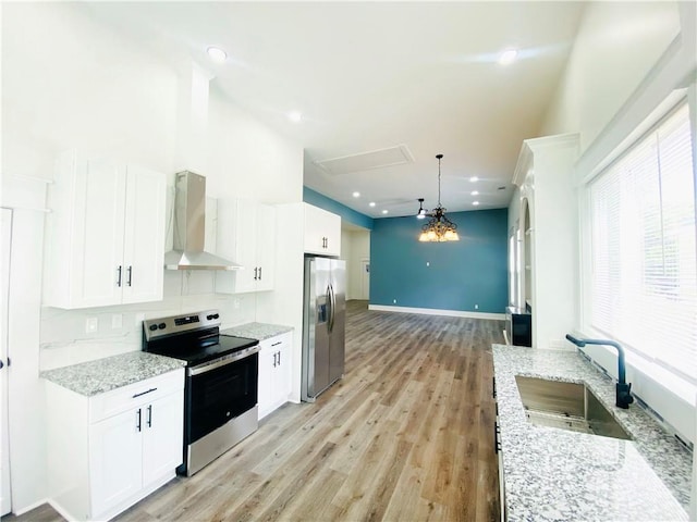 kitchen featuring white cabinets, wall chimney range hood, sink, decorative light fixtures, and stainless steel appliances