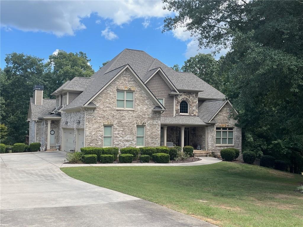 8440 Woodland Brooke Trl, Cumming, GA 30028 - view of front facade with driveway, roof with shingles, a front yard, a chimney, and an attached garage