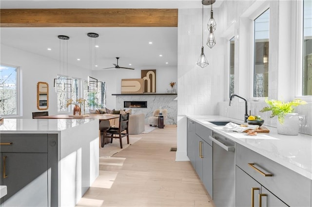 kitchen with gray cabinetry, a fireplace, decorative light fixtures, stainless steel dishwasher, and light wood-type flooring