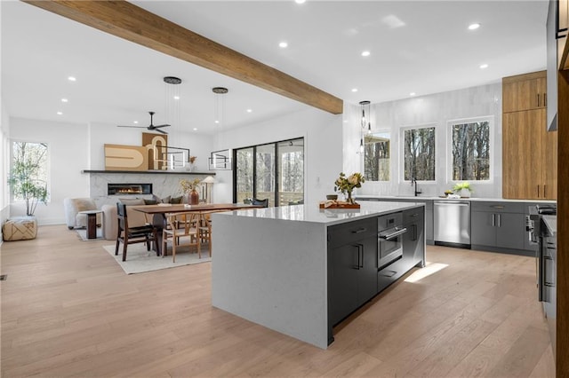 kitchen with beamed ceiling, a center island, light hardwood / wood-style flooring, appliances with stainless steel finishes, and pendant lighting