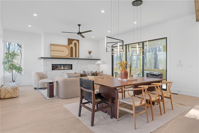 dining area with a fireplace, light hardwood / wood-style floors, and ceiling fan