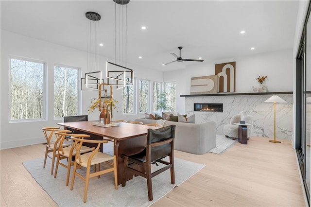 dining space with a fireplace, ceiling fan, and light wood-type flooring