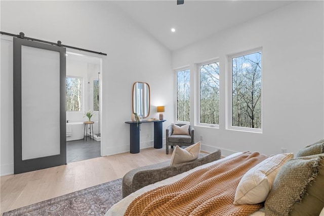 bedroom with hardwood / wood-style flooring, connected bathroom, a barn door, and high vaulted ceiling